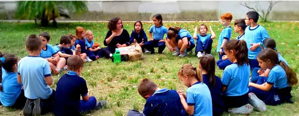 Chicos de primaria en ronda sobre el pasto, con la maestra